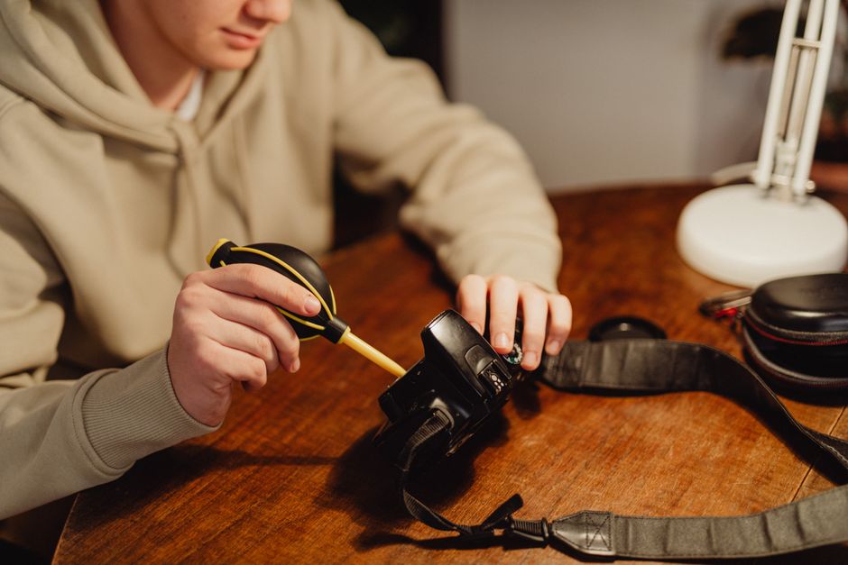 Person cleaning a camera lens on a wooden table